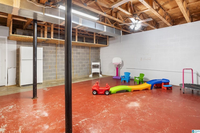 basement featuring a ceiling fan, freestanding refrigerator, and concrete block wall