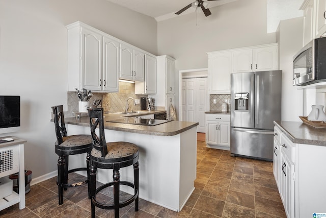 kitchen featuring a kitchen breakfast bar, a peninsula, stainless steel appliances, white cabinetry, and a sink