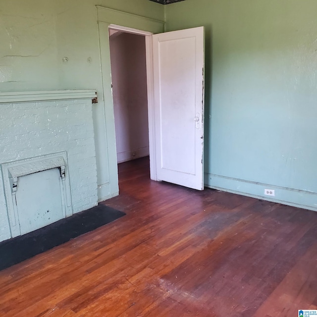 spare room featuring dark wood-type flooring and a brick fireplace