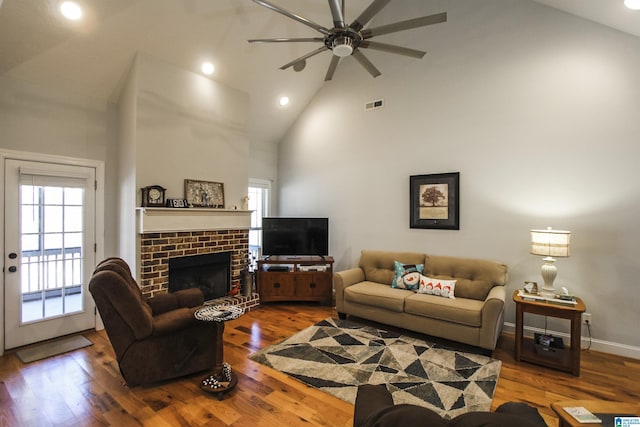 living room featuring visible vents, a brick fireplace, wood finished floors, high vaulted ceiling, and baseboards