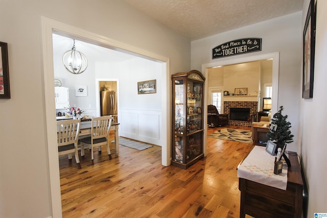 corridor featuring a wainscoted wall, a notable chandelier, a decorative wall, a textured ceiling, and wood finished floors