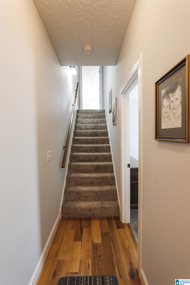 stairs featuring a textured ceiling, wood finished floors, and baseboards