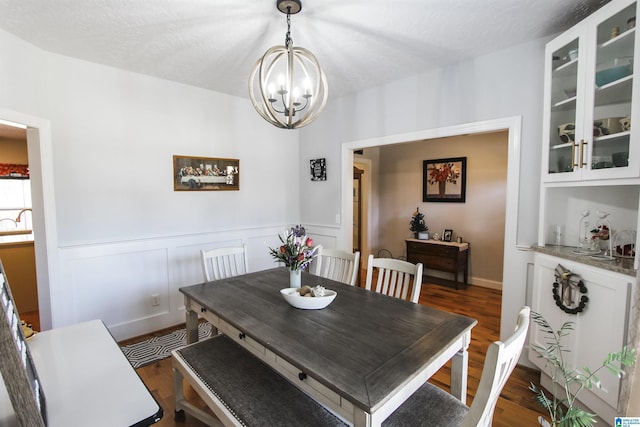 dining space with dark wood-type flooring, a chandelier, wainscoting, and a textured ceiling