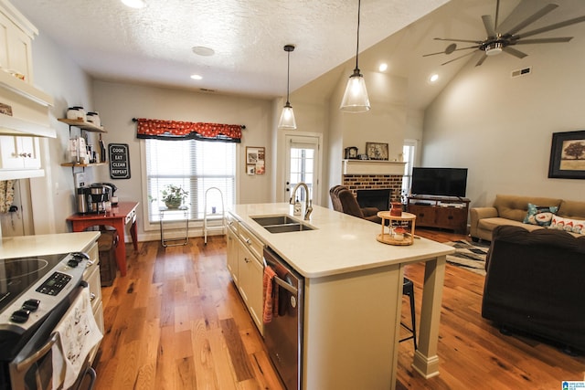 kitchen featuring an island with sink, appliances with stainless steel finishes, hanging light fixtures, light countertops, and a sink