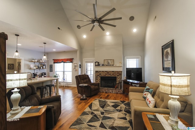 living room featuring visible vents, a brick fireplace, ceiling fan, wood finished floors, and high vaulted ceiling