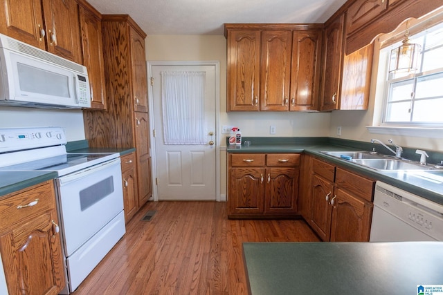 kitchen featuring white appliances, dark countertops, brown cabinets, light wood-type flooring, and a sink