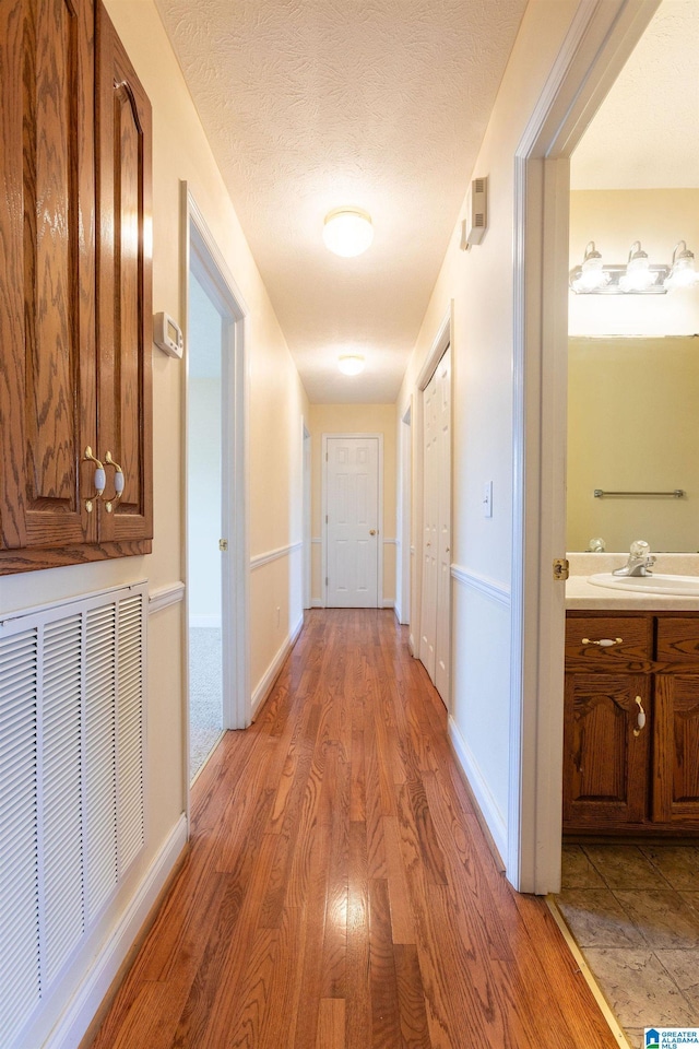 corridor featuring visible vents, a sink, a textured ceiling, wood finished floors, and baseboards