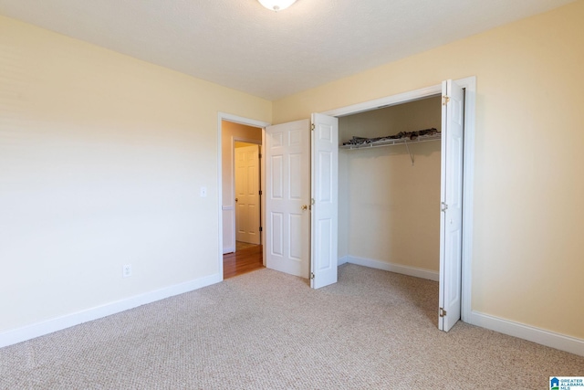 unfurnished bedroom featuring baseboards, a closet, and light colored carpet