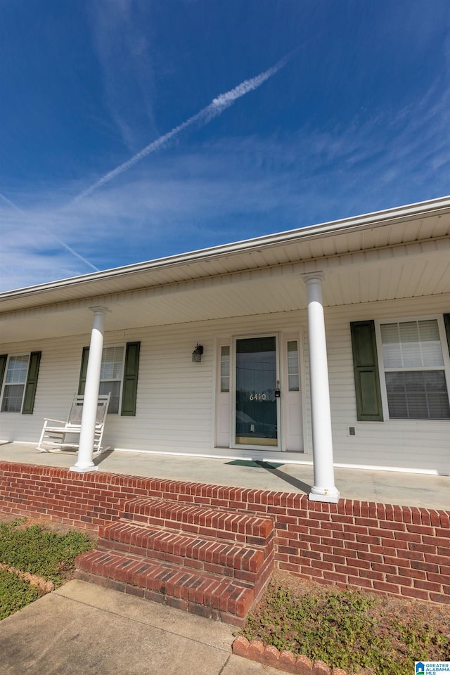 doorway to property with covered porch and brick siding