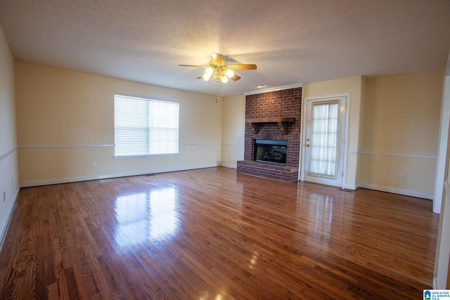 unfurnished living room with ceiling fan, a textured ceiling, baseboards, a brick fireplace, and dark wood finished floors