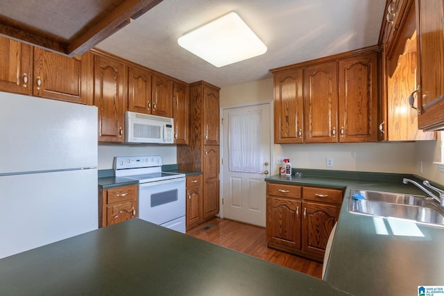 kitchen featuring dark countertops, white appliances, brown cabinets, and a sink