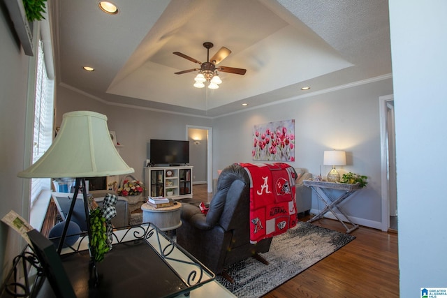 living room with baseboards, dark wood finished floors, ceiling fan, ornamental molding, and a tray ceiling