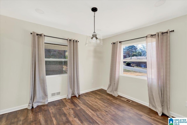 spare room with dark wood-type flooring, visible vents, and baseboards