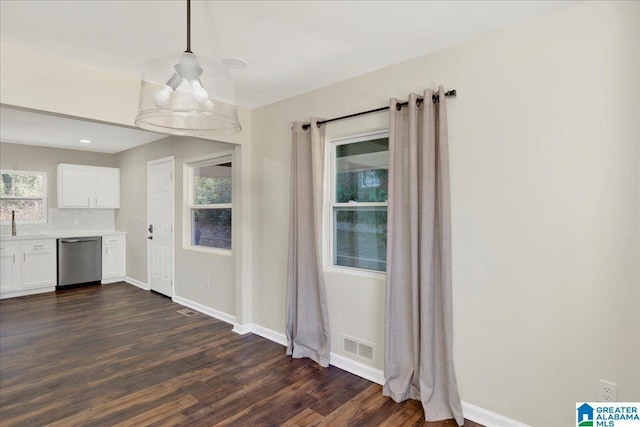 unfurnished dining area featuring dark wood-style flooring, a sink, visible vents, and baseboards