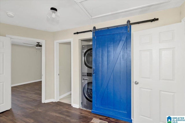 laundry room featuring laundry area, a barn door, baseboards, dark wood-type flooring, and stacked washing maching and dryer