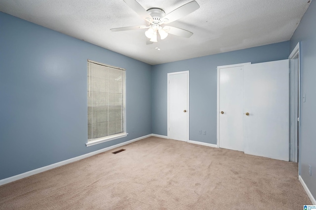 unfurnished bedroom with a textured ceiling, ceiling fan, light colored carpet, visible vents, and baseboards