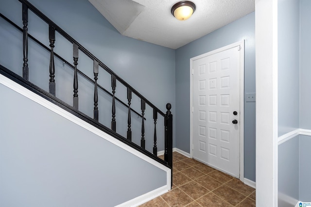 foyer entrance with stairs, dark tile patterned floors, a textured ceiling, and baseboards