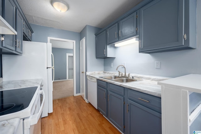 kitchen featuring light countertops, a sink, wall chimney range hood, blue cabinets, and white appliances