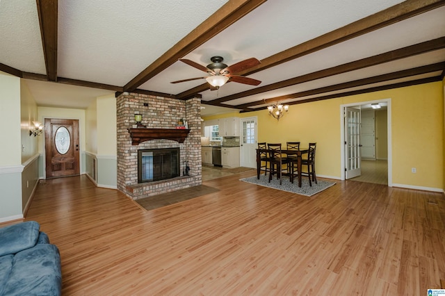 living room featuring beam ceiling, a fireplace, light wood-style flooring, a textured ceiling, and baseboards