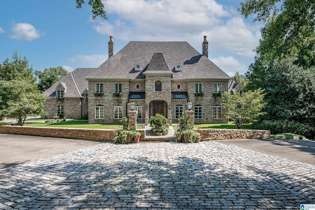 french country style house featuring a chimney, decorative driveway, and a front yard