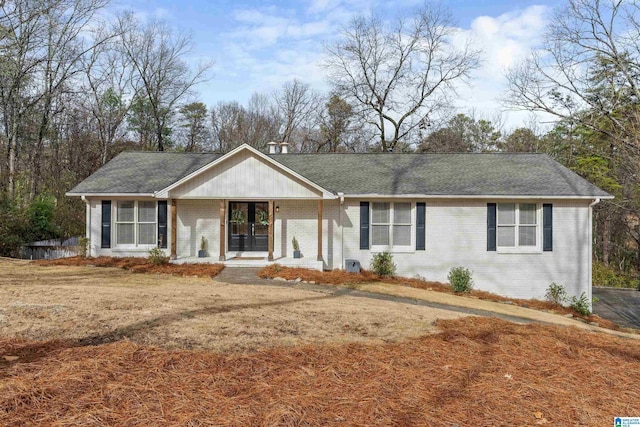 ranch-style home with a shingled roof, covered porch, and brick siding