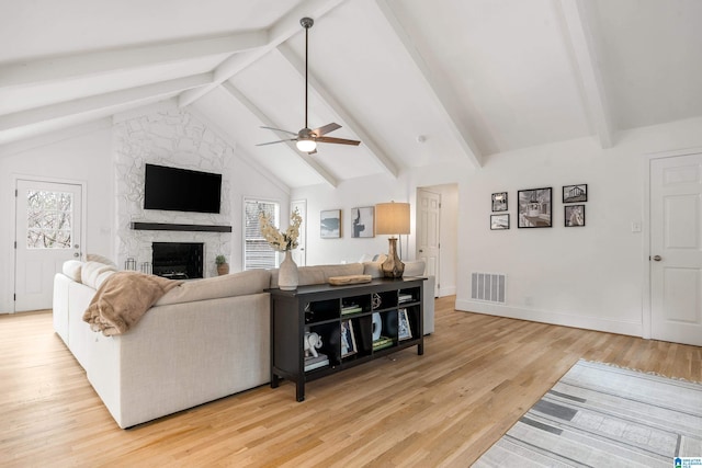 living area with light wood finished floors, plenty of natural light, visible vents, and a stone fireplace