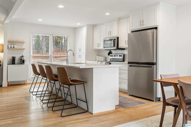 kitchen with stainless steel appliances, a sink, white cabinets, light wood-style floors, and an island with sink