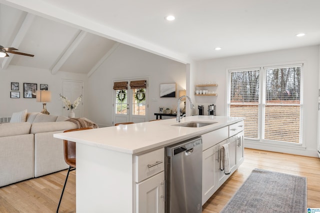 kitchen with lofted ceiling with beams, light wood-style flooring, open floor plan, stainless steel dishwasher, and a sink