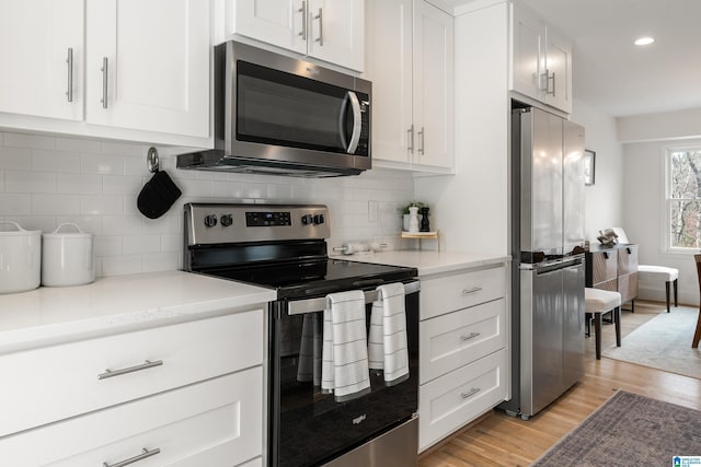 kitchen with appliances with stainless steel finishes, white cabinets, light wood-style flooring, and tasteful backsplash