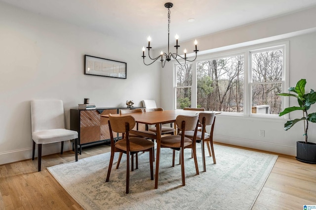 dining space featuring baseboards, an inviting chandelier, and light wood-style floors