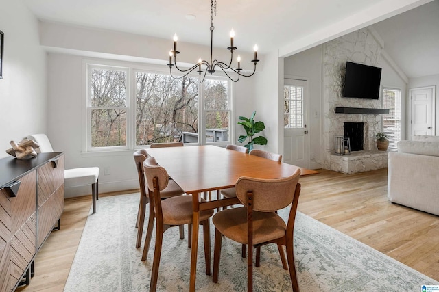 dining area featuring a fireplace, lofted ceiling, a chandelier, light wood-type flooring, and baseboards