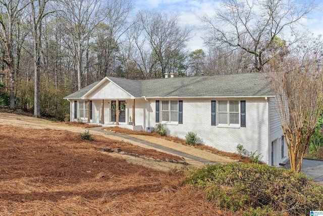 ranch-style house with brick siding, roof with shingles, a porch, an attached garage, and driveway