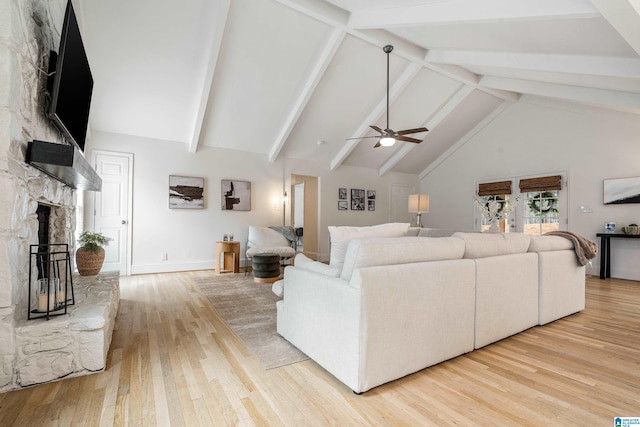 living room featuring ceiling fan, high vaulted ceiling, a stone fireplace, beam ceiling, and light wood finished floors