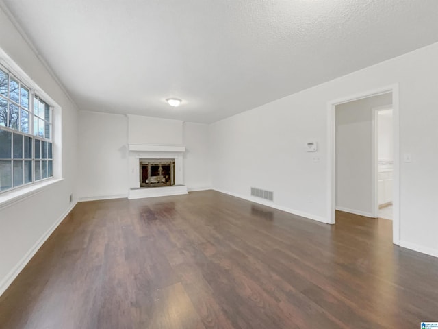 unfurnished living room featuring baseboards, visible vents, a fireplace with raised hearth, and dark wood-type flooring