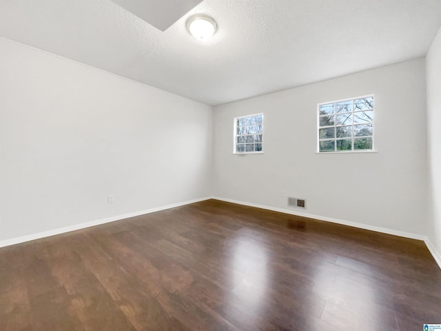 spare room featuring baseboards, a textured ceiling, visible vents, and dark wood-style flooring