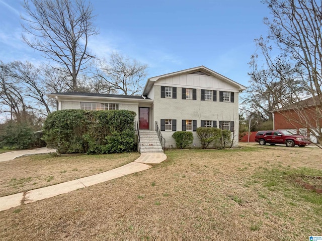 split level home featuring board and batten siding, a front yard, and brick siding