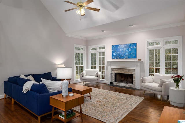 living area with dark wood-style floors, crown molding, a stone fireplace, and a ceiling fan