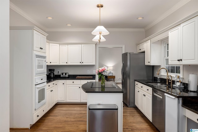 kitchen featuring dark countertops, a kitchen island, appliances with stainless steel finishes, white cabinetry, and a sink