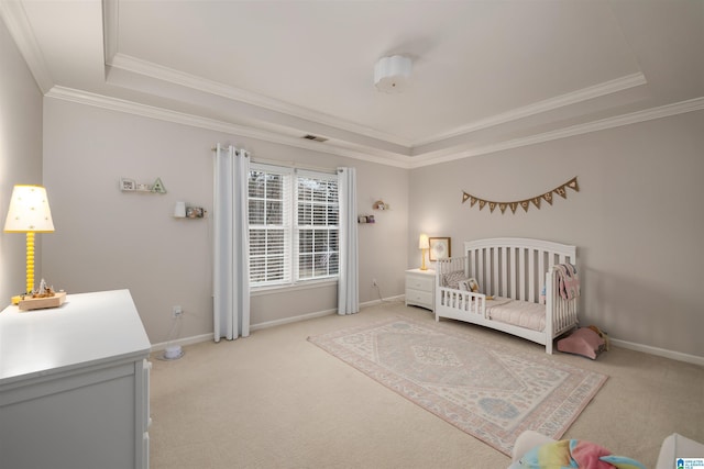 bedroom with a crib, light colored carpet, baseboards, a tray ceiling, and crown molding