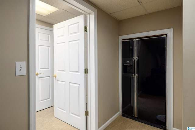 hallway featuring baseboards, light carpet, and a drop ceiling