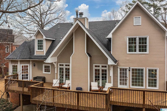 rear view of property with a shingled roof, a chimney, and a deck