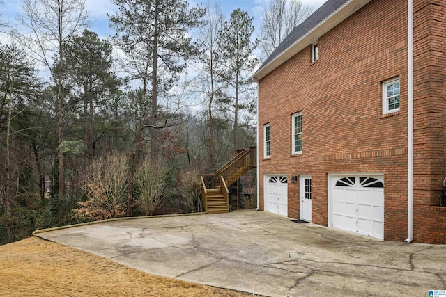 view of side of home with a garage, brick siding, driveway, and stairway