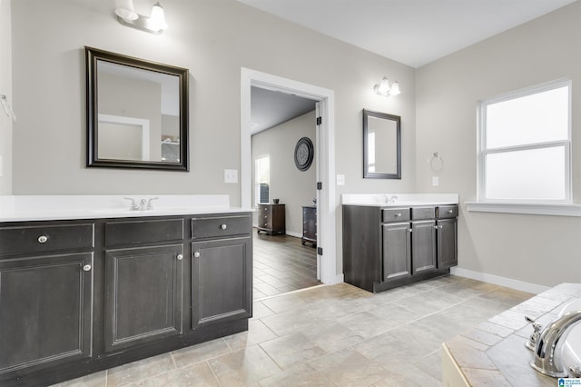 bathroom featuring two vanities, a sink, and baseboards