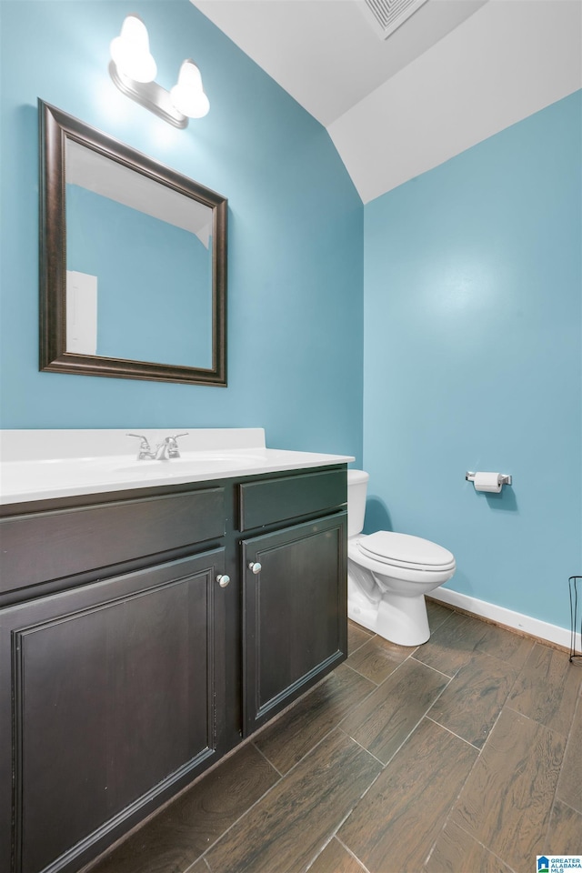 half bath featuring toilet, wood finish floors, vanity, baseboards, and vaulted ceiling