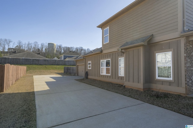 exterior space featuring concrete driveway, a patio, a fenced backyard, board and batten siding, and brick siding