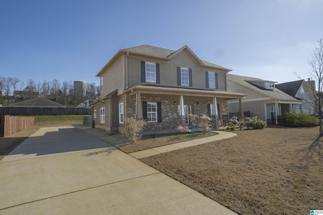 view of front of property with a porch, brick siding, fence, and a front lawn