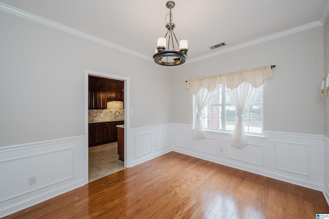 unfurnished dining area featuring light wood-style floors, wainscoting, visible vents, and an inviting chandelier