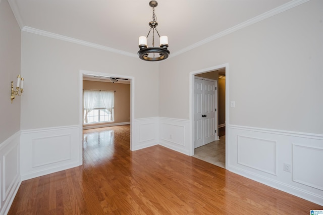 unfurnished dining area featuring a chandelier, ornamental molding, a wainscoted wall, and wood finished floors