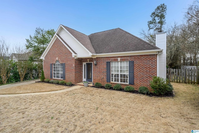 traditional home with roof with shingles, a front yard, fence, and brick siding