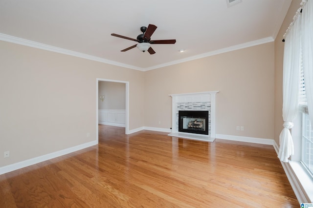 unfurnished living room featuring crown molding, a tiled fireplace, light wood-style floors, ceiling fan, and baseboards